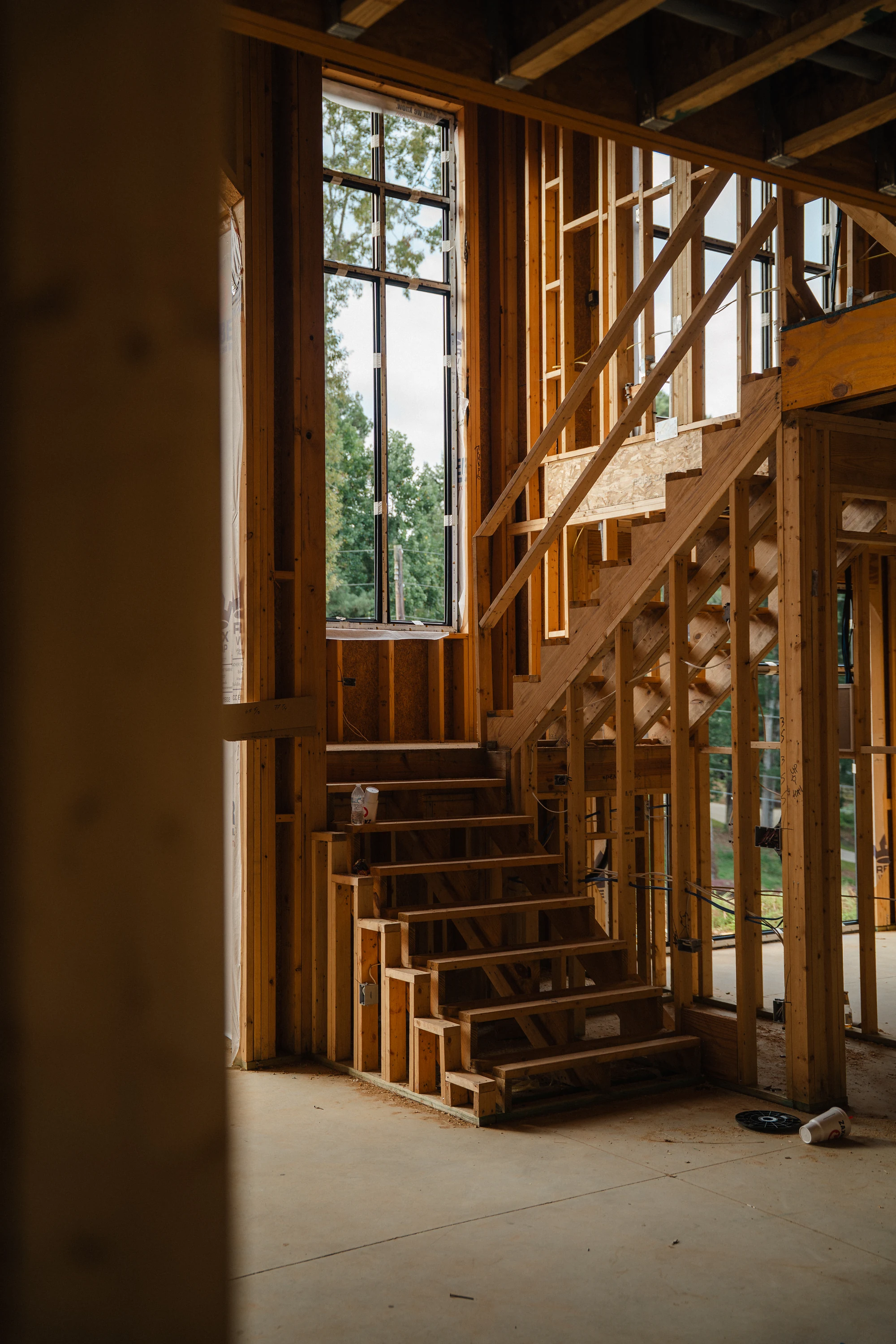 Vertical view of unfinished wood stairs rising beside open stud walls and tall windows.